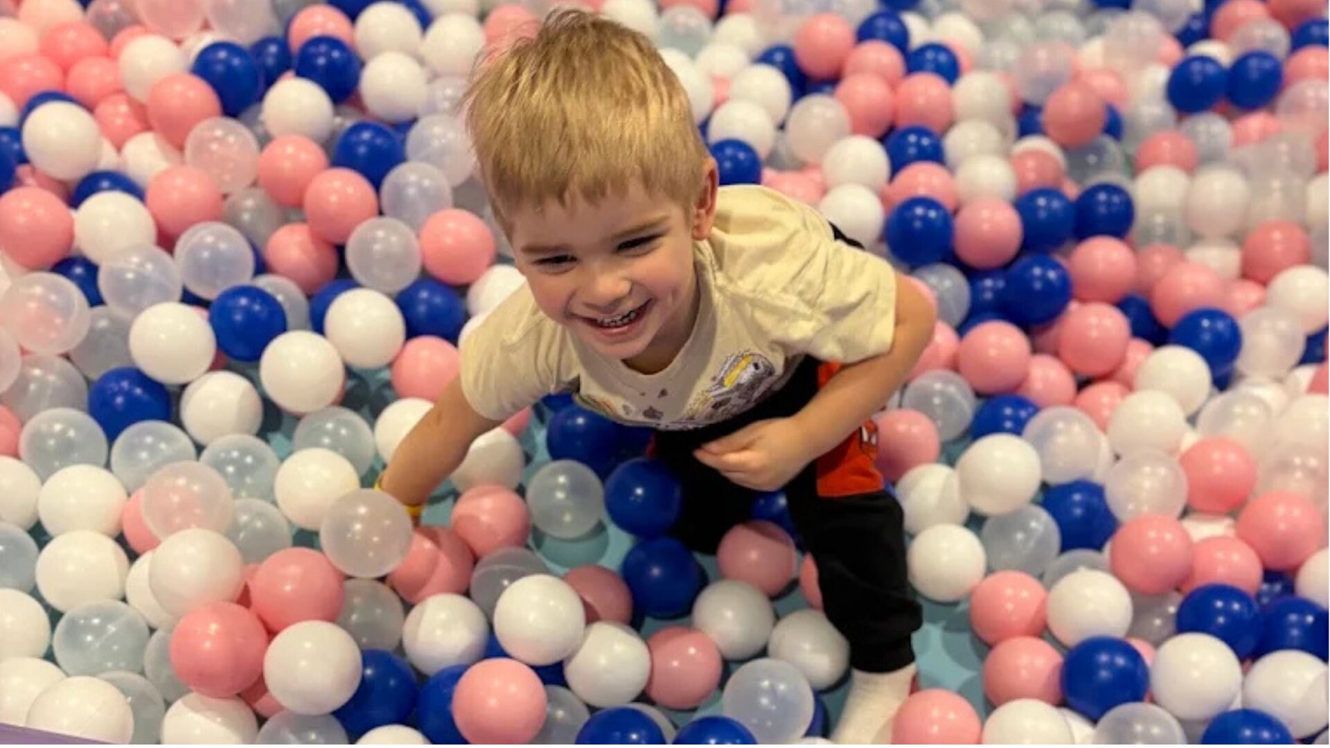 A young boy playing and smiling in the ball pit at Hyper Kidz Wheaton